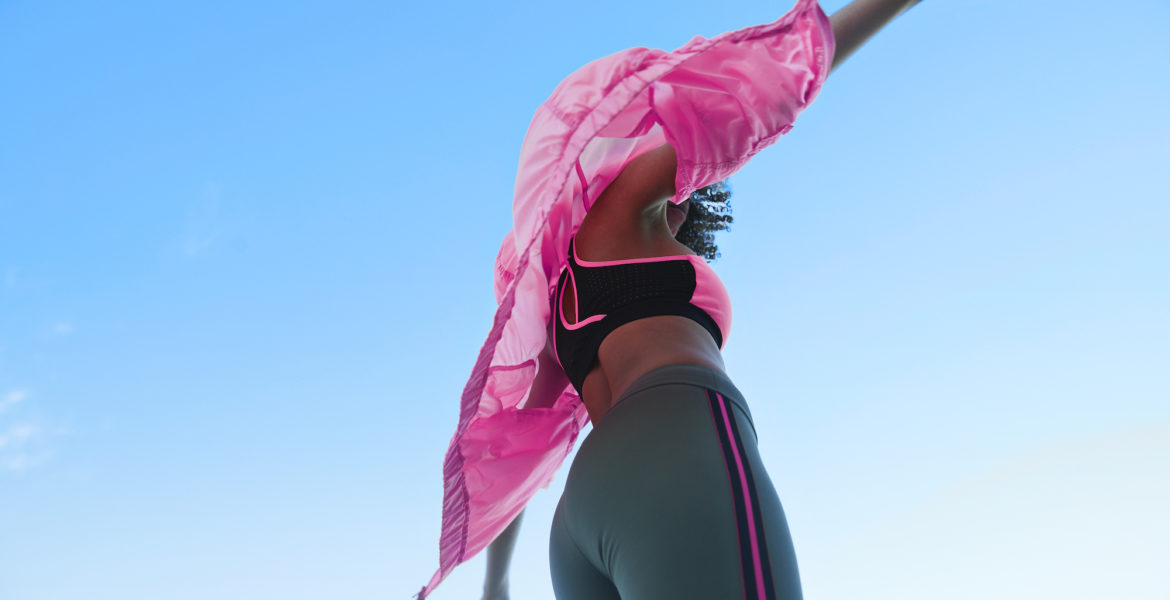 Fashionable female athlete wearing jacket with sport clothing against clear blue sky