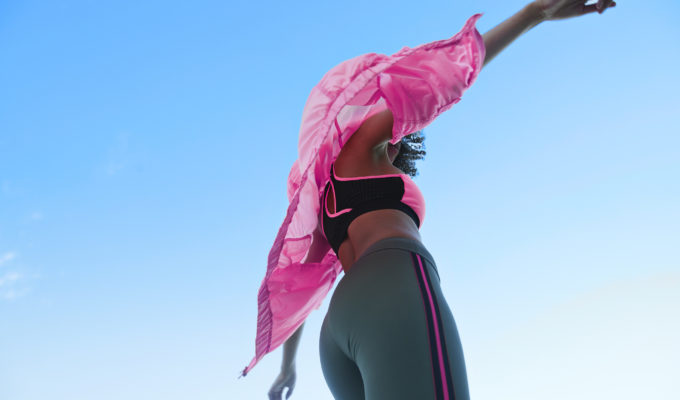 Fashionable female athlete wearing jacket with sport clothing against clear blue sky